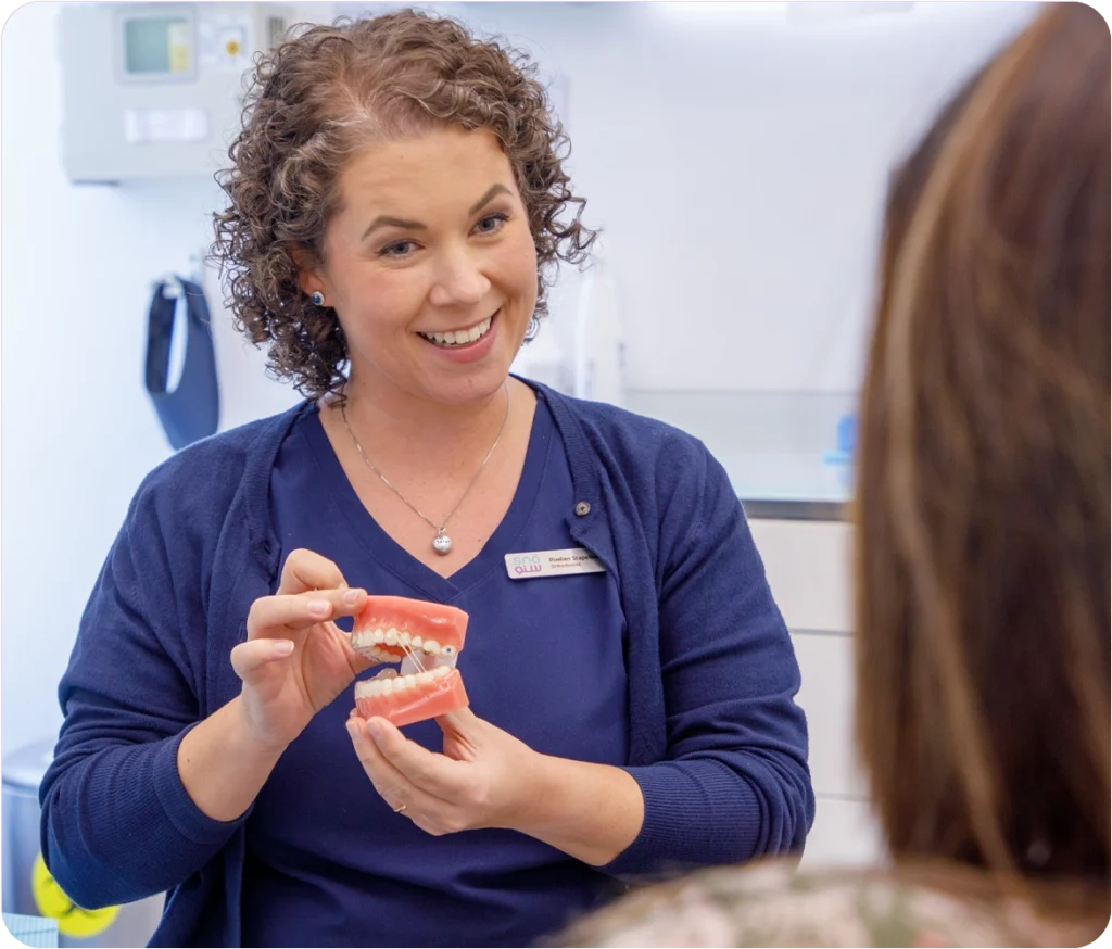 dr roelien stapelberg with patient - Snö Clinics | Abu Dhabi Dentist showing proper flossing technique for maintaining oral hygiene with a fixed retainer.