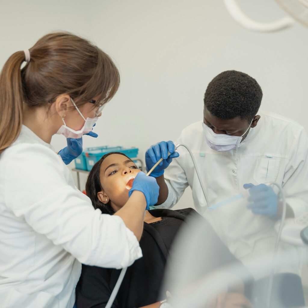 Dentist and assistant in masks and gloves working on a patient seated in a dental chair.